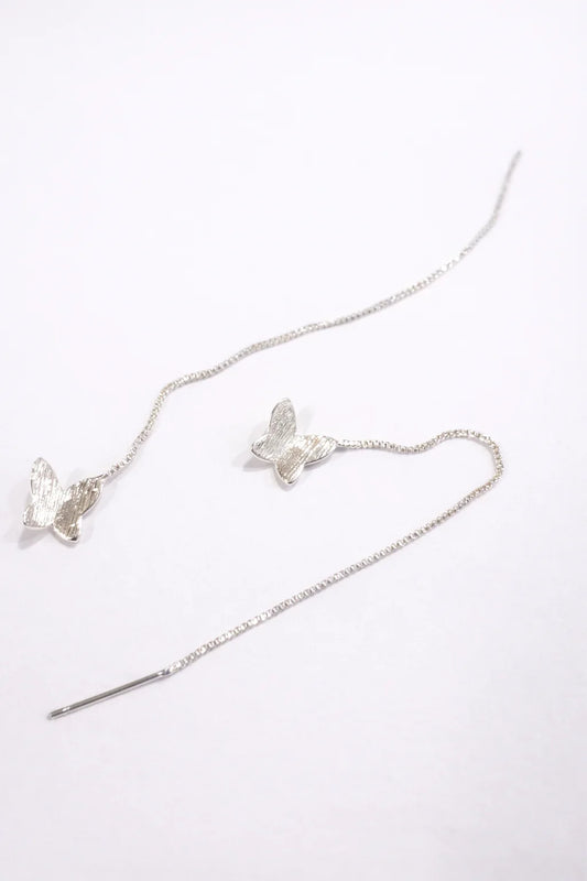 Boucles d'oreilles argentées pendantes avec motifs papillon texturé sur fond blanc