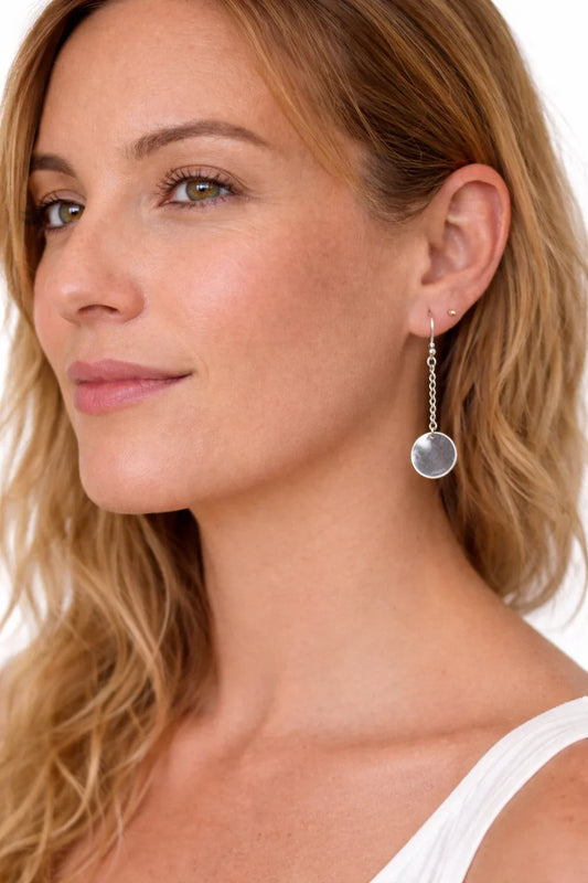 Femme blonde souriante portant une boucle d'oreille argentée pendante ronde