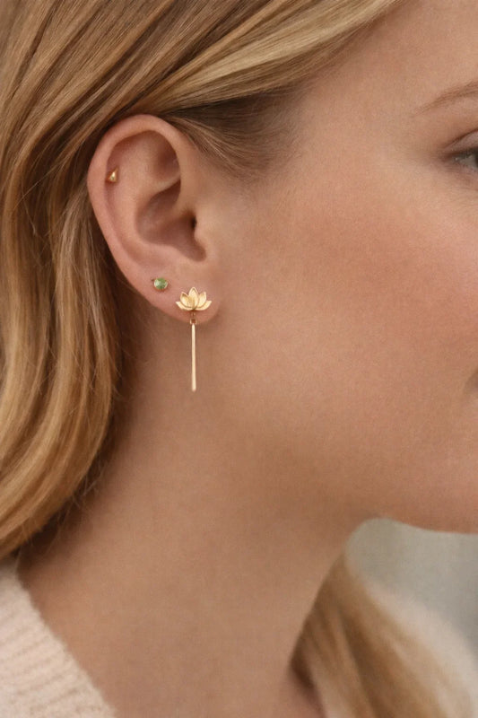 Oreille féminine avec trois boucles d'oreilles en or, dont une fleur de lotus avec pendant long