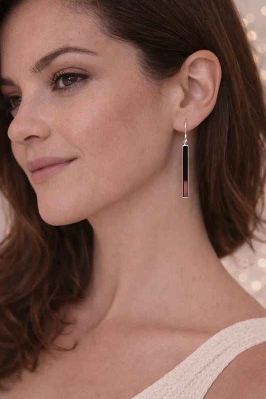 Femme portant une boucle d'oreille barre longue noire et argent sur fond clair flou