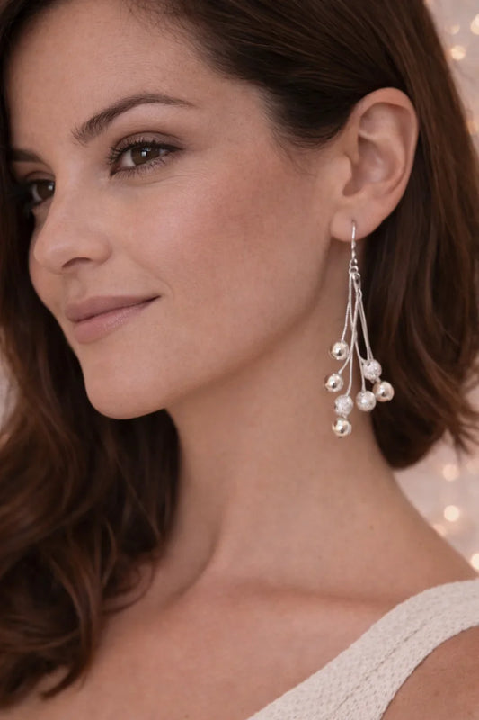 Femme portant une boucle d'oreille argentée avec boules décoratives pendantes, fond lumineux festif.
