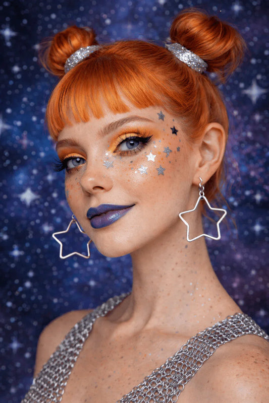 Portrait d'une femme rousse avec maquillage étoilé, boucles d'oreilles étoiles et argent fond de fête bleu