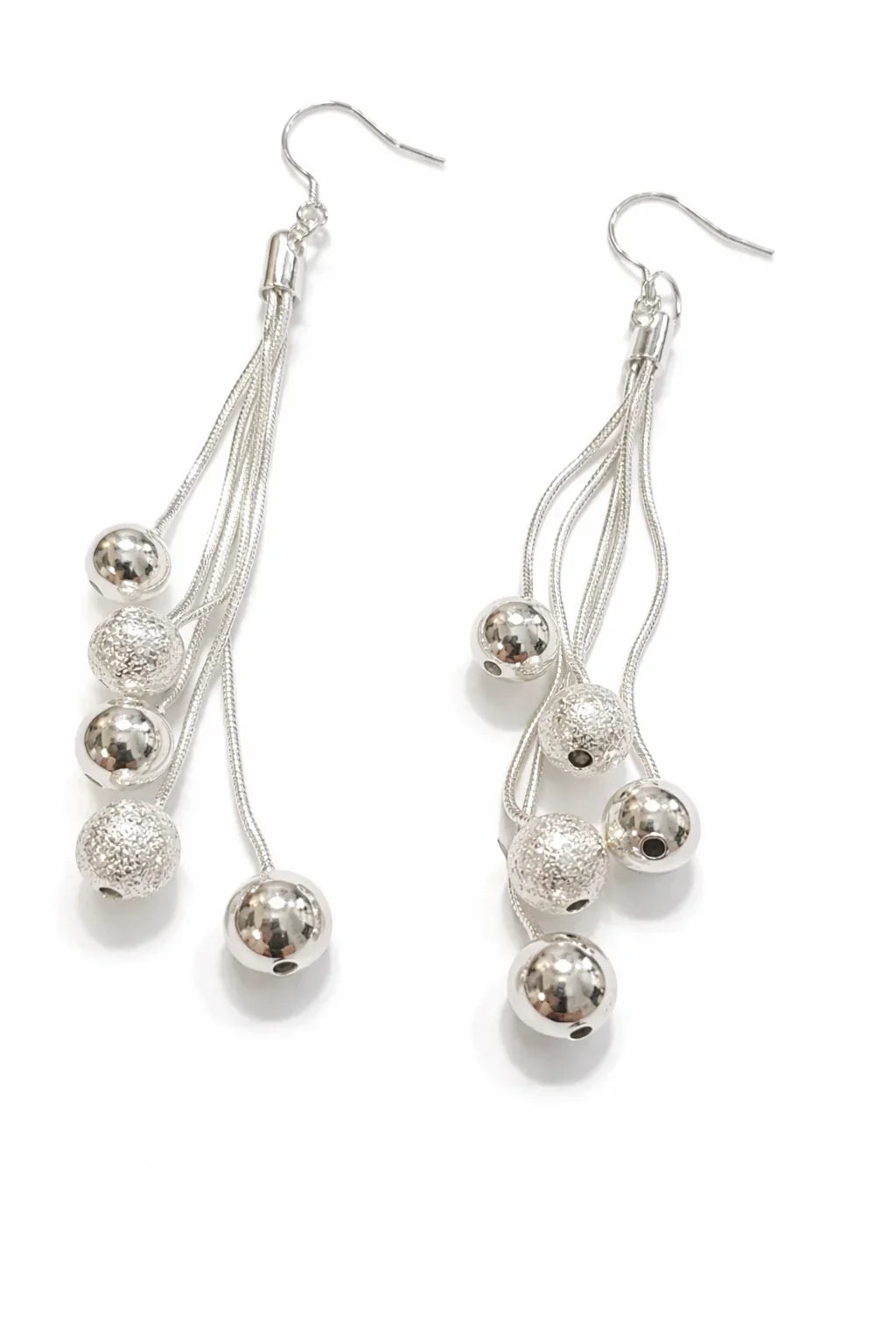 Boucles d'oreilles argentées pendantes avec perles brillantes et texturées sur fond blanc