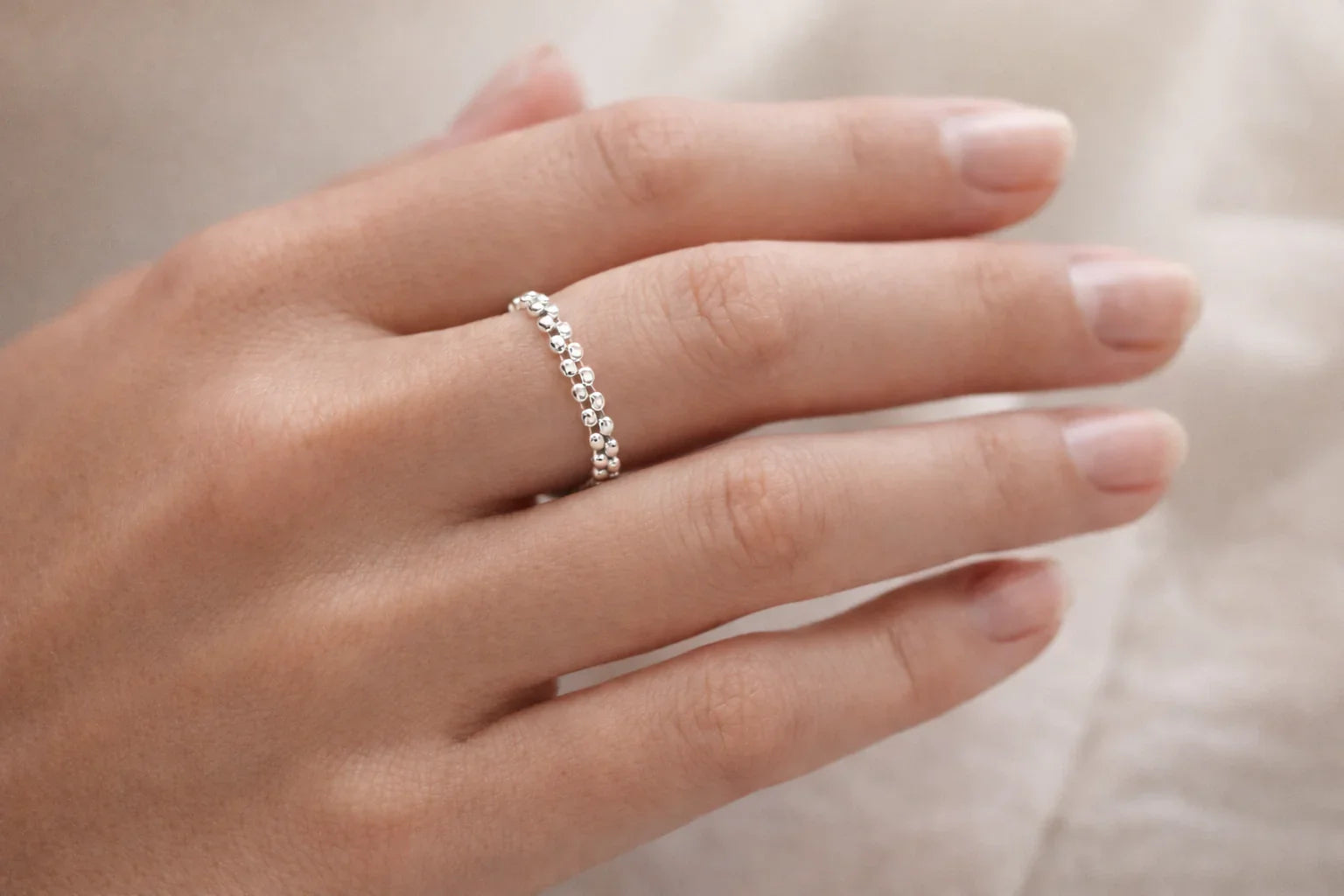 Main de femme avec bague argentée à billes, peau claire, fond neutre flou