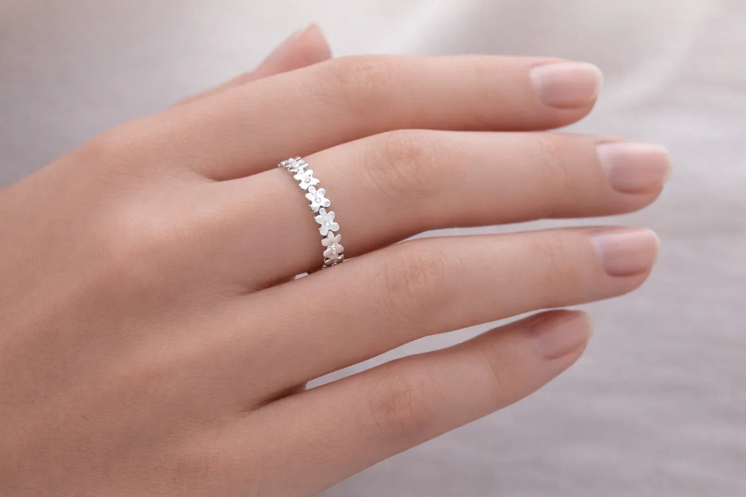 Main de femme avec bague argentée à fleurs fines sur l'annulaire, fond gris clair