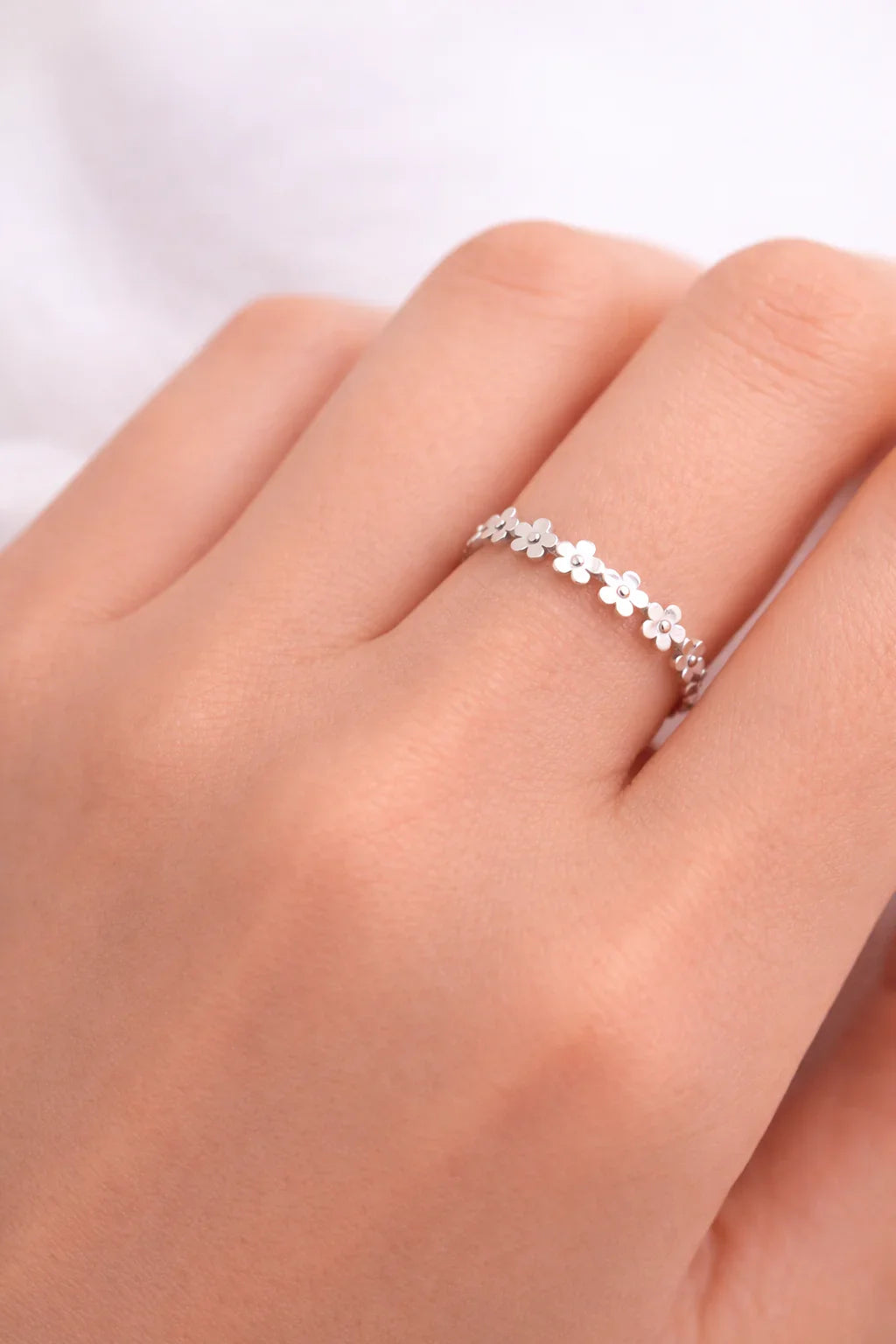 Main sur fond clair avec bague argentée à motif de petites fleurs