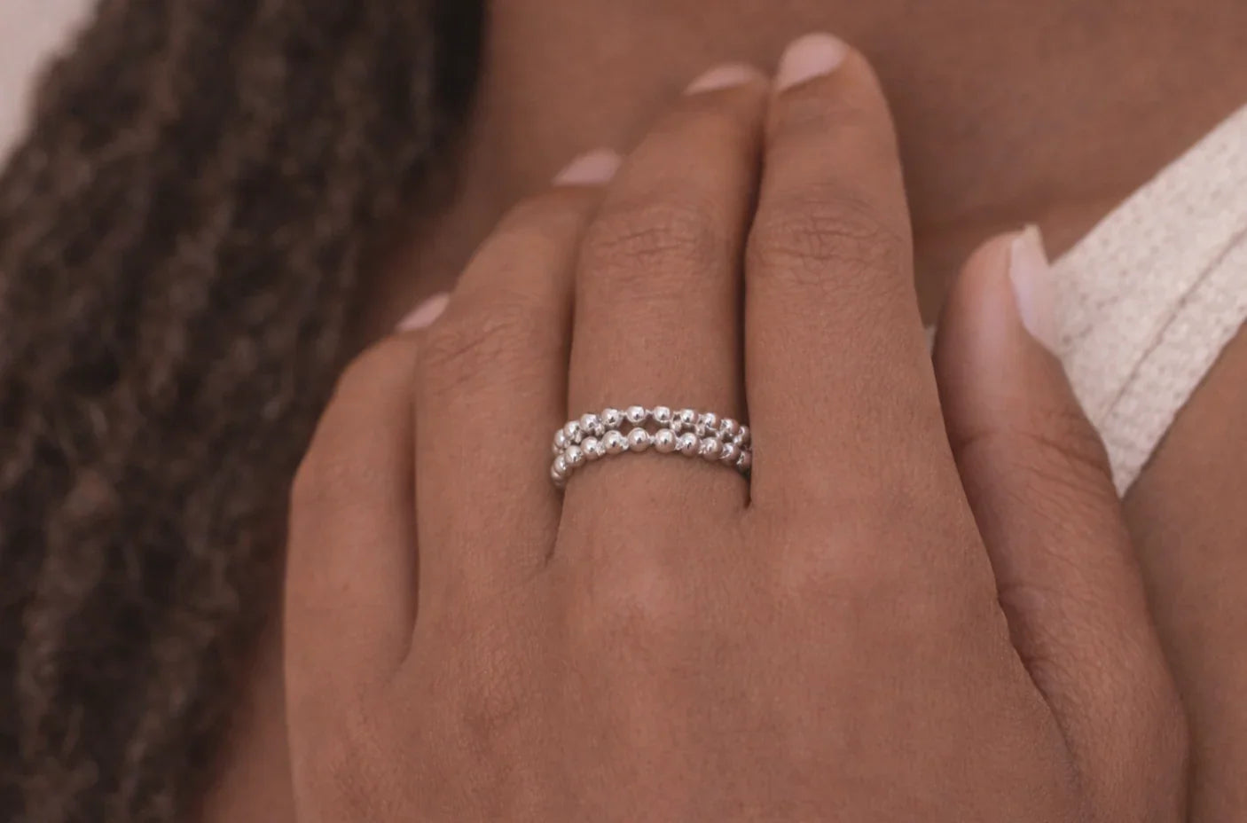 Main féminine avec bague argent à deux rangées de perles sur la main, peau foncée, fond flou