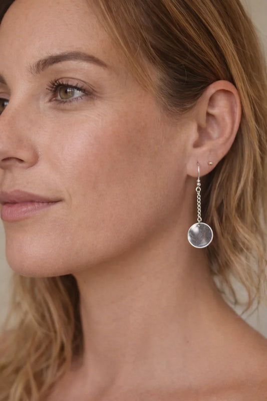 Femme portant une boucle d'oreille pendante argentée avec un disque rond, portrait en gros plan